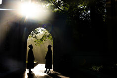 Silhouettes of a male and female graduate facing each other in an archway with sun rays in the background.